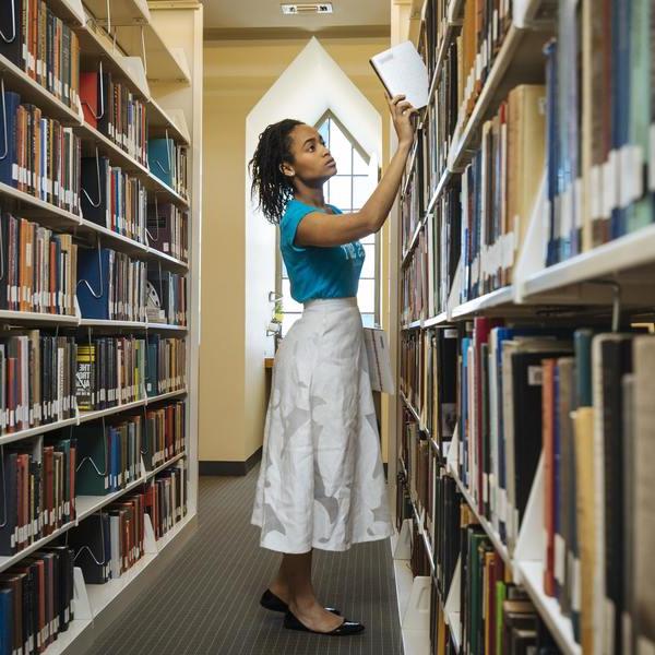 a female student pulling a book from a library shelf